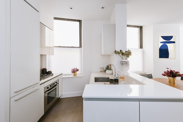 kitchen featuring stainless steel appliances, light countertops, white cabinetry, dark wood-style flooring, and a sink