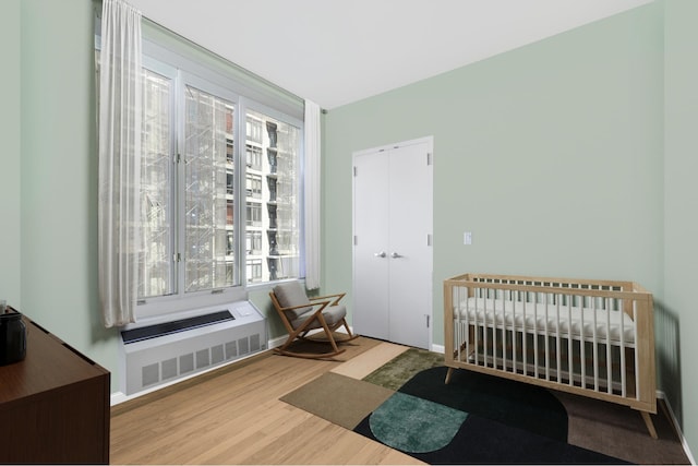 bedroom featuring radiator heating unit, wood finished floors, a closet, baseboards, and a crib