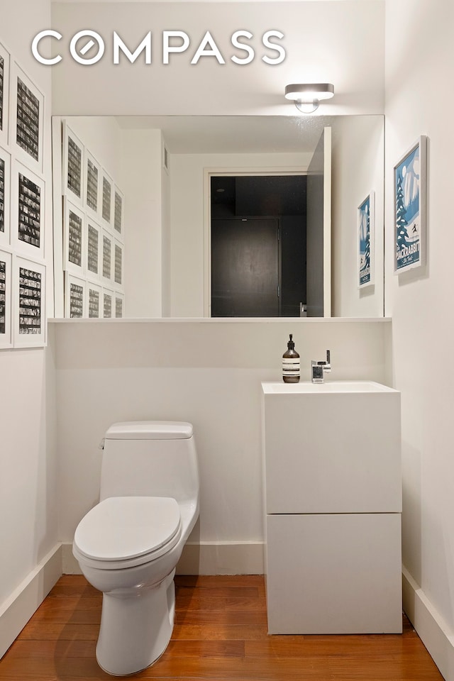 bathroom featuring toilet, wood finished floors, baseboards, and vanity