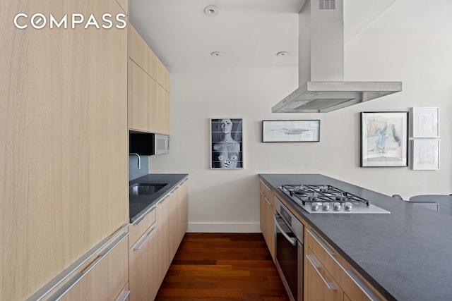 kitchen featuring stainless steel appliances, wall chimney exhaust hood, dark wood-type flooring, and light brown cabinetry
