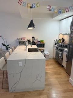 kitchen featuring a sink, black gas stove, light wood-type flooring, decorative light fixtures, and light stone countertops
