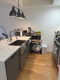 kitchen featuring stainless steel microwave, a sink, light wood-type flooring, gray cabinets, and light stone counters