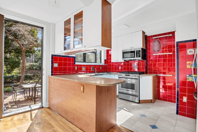 39-39 46th St, New York City, NY 11104 - kitchen featuring appliances with stainless steel finishes, a sink, a peninsula, white cabinetry, and glass insert cabinets