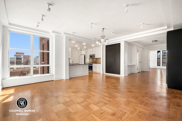 unfurnished living room with an inviting chandelier, baseboards, and a tray ceiling