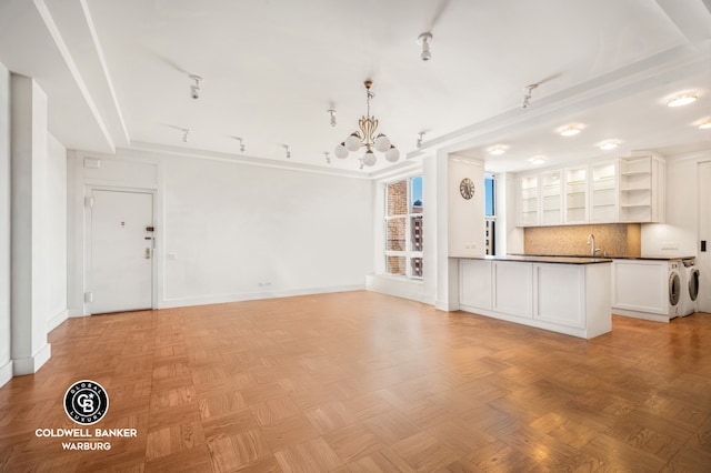 unfurnished living room with a sink, washer and dryer, baseboards, and a chandelier