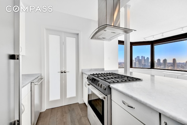 kitchen with island exhaust hood, gas range, white cabinets, and a view of skyline