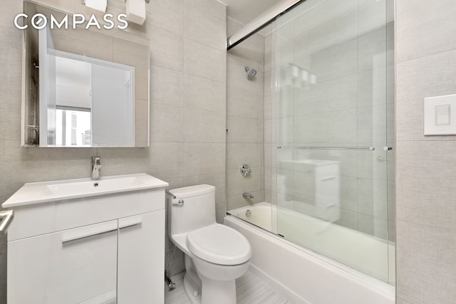 bathroom featuring tile walls, combined bath / shower with glass door, toilet, and vanity