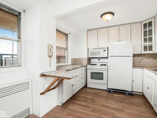 5800 Arlington Ave Unit 7L, New York City, NY 10471 - kitchen with white appliances, radiator heating unit, backsplash, glass insert cabinets, and light wood-style flooring