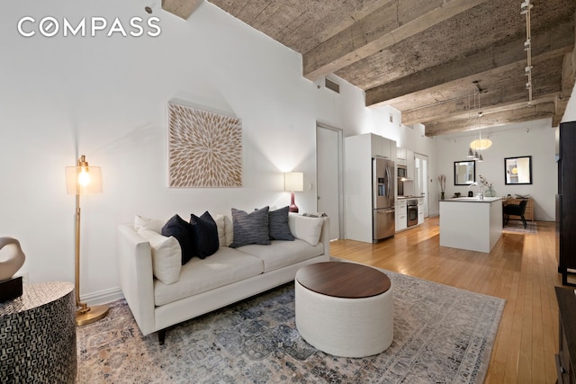 living area with beamed ceiling, light wood-style floors, and visible vents