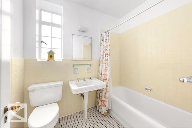 full bathroom featuring wainscoting, toilet, tile walls, a sink, and shower / tub combo