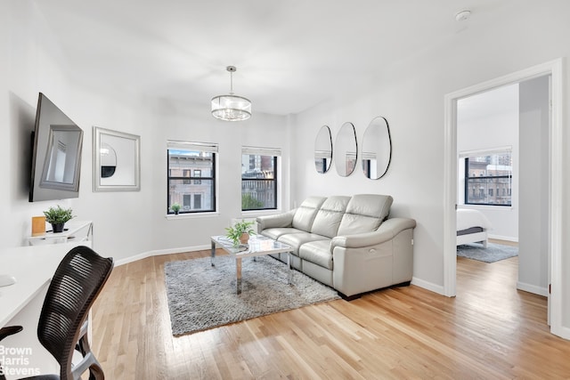 living room featuring light wood-type flooring, a chandelier, and baseboards