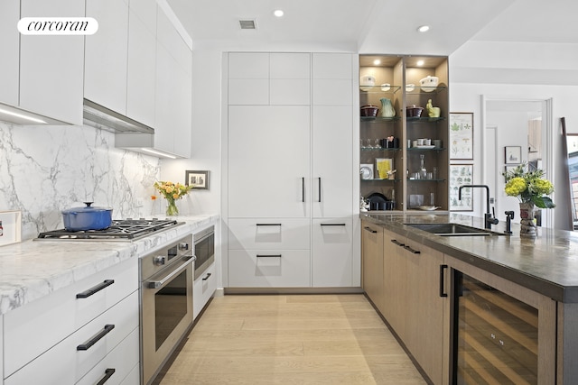 kitchen with stainless steel appliances, beverage cooler, a sink, modern cabinets, and light wood finished floors