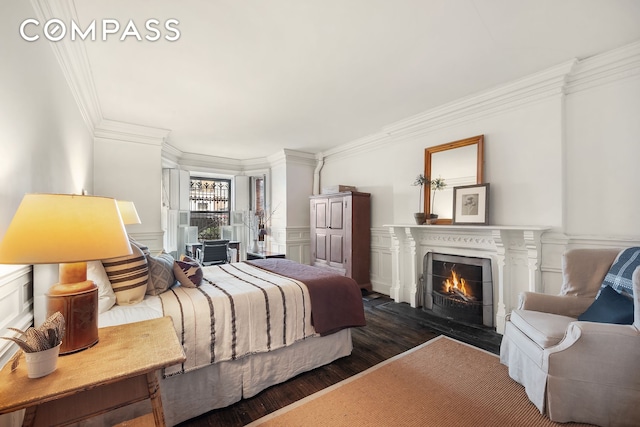 bedroom featuring dark wood finished floors, a warm lit fireplace, and crown molding