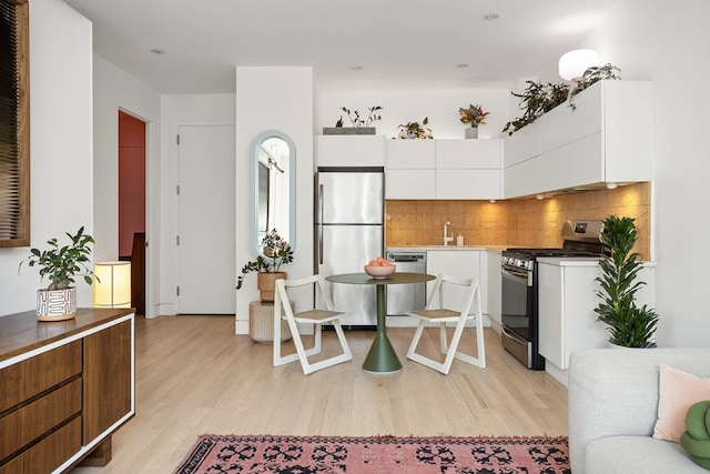 kitchen featuring light wood-style floors, appliances with stainless steel finishes, backsplash, and white cabinetry