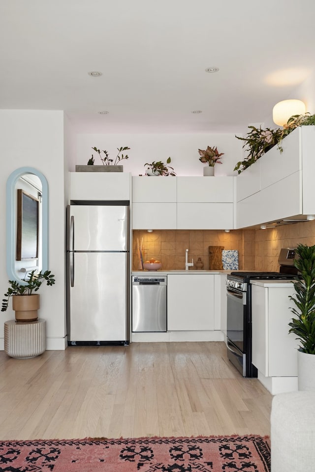 kitchen with backsplash, modern cabinets, light wood-type flooring, white cabinets, and stainless steel appliances