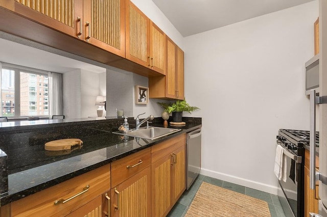 kitchen featuring dark tile patterned floors, baseboards, dark stone countertops, stainless steel appliances, and a sink