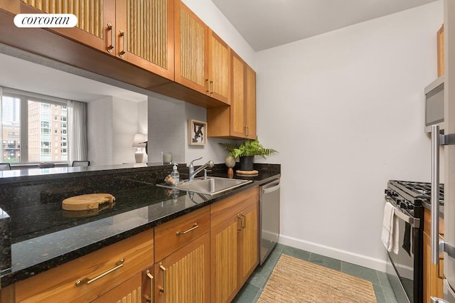 kitchen featuring dark tile patterned floors, baseboards, dark stone countertops, stainless steel appliances, and a sink