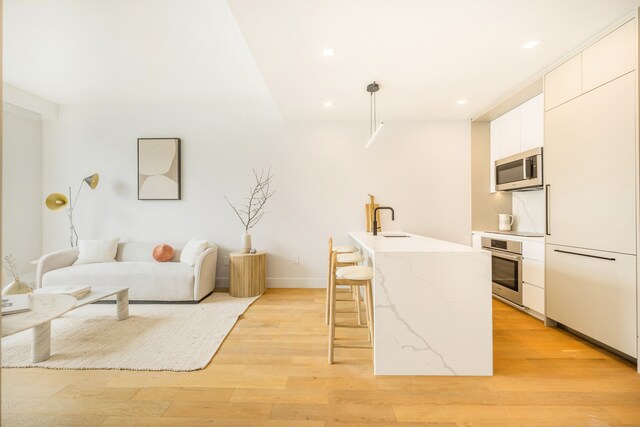 37-34 33rd St Unit 3-K, New York City, NY 11101 - kitchen featuring stainless steel appliances, modern cabinets, a kitchen breakfast bar, a sink, and light wood-style floors