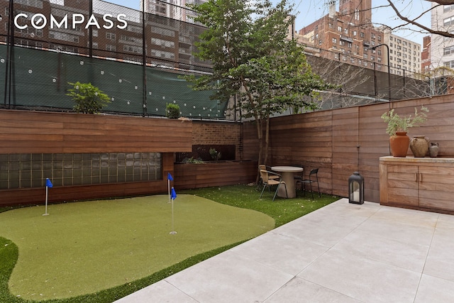 view of yard with an area to practice putting, fence, and a patio area