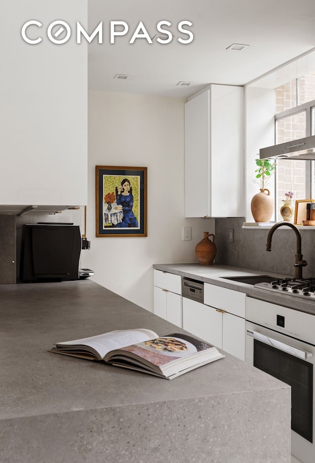 kitchen with white oven, modern cabinets, white cabinetry, and tasteful backsplash