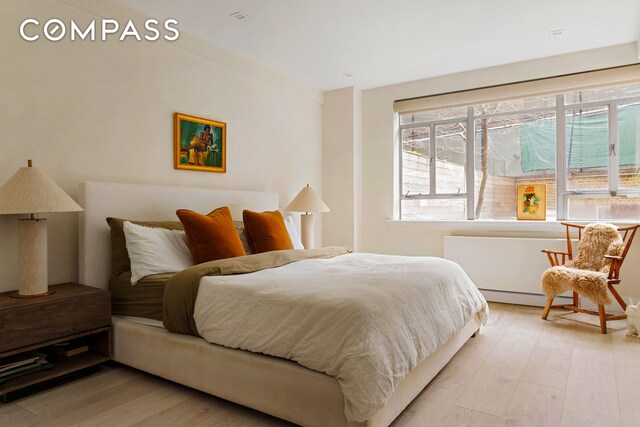 bedroom featuring multiple windows, light wood finished floors, and a baseboard heating unit