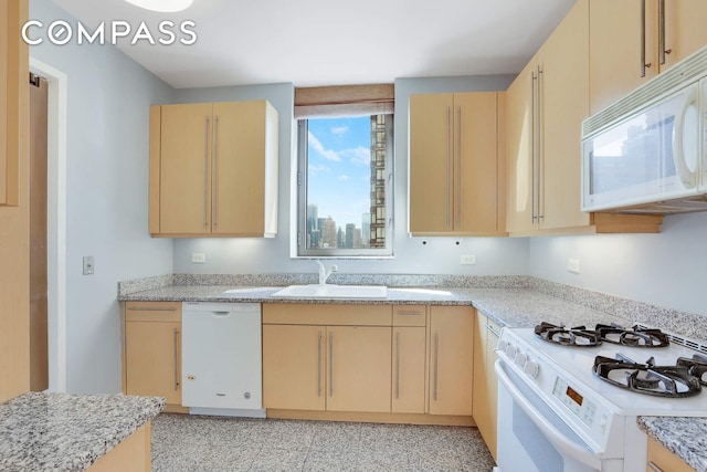 kitchen with white appliances, light brown cabinetry, light stone counters, and a sink