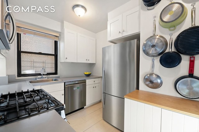 kitchen featuring appliances with stainless steel finishes, a sink, light tile patterned floors, light countertops, and white cabinetry