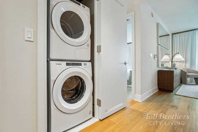 laundry area featuring stacked washing maching and dryer, laundry area, baseboards, and wood finished floors