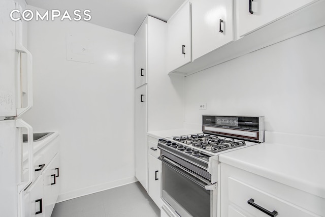kitchen featuring gas stove, baseboards, light countertops, freestanding refrigerator, and white cabinets