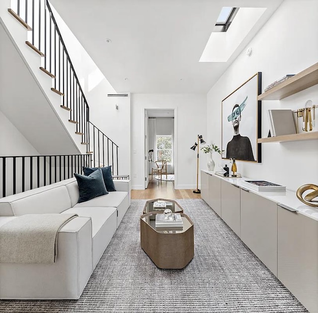 living area featuring a skylight, light wood-style floors, and stairs