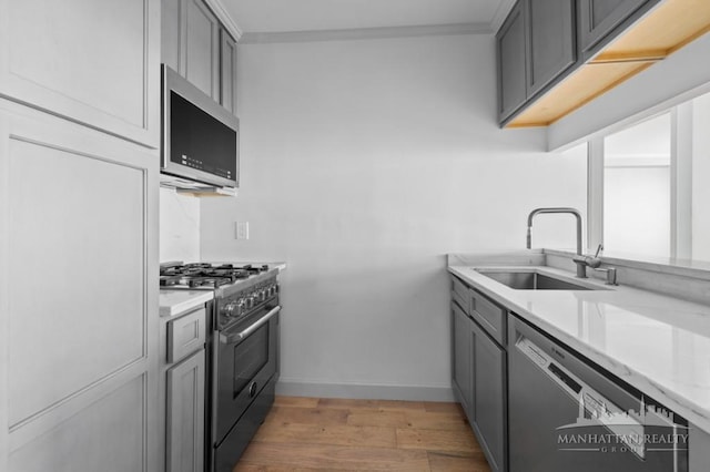 kitchen featuring stainless steel appliances, a sink, gray cabinetry, light wood-style floors, and light countertops