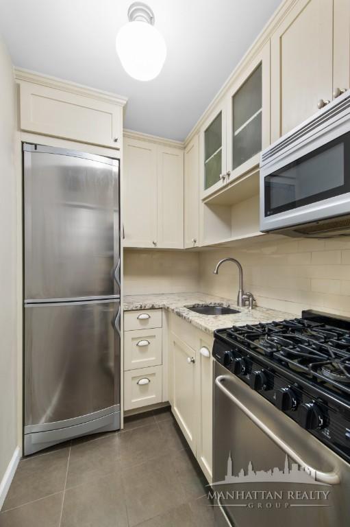 kitchen with light stone counters, a sink, dark tile patterned flooring, appliances with stainless steel finishes, and cream cabinets