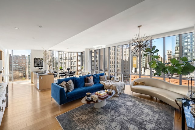 living area with light wood-type flooring, healthy amount of natural light, a chandelier, a view of city, and a wall of windows