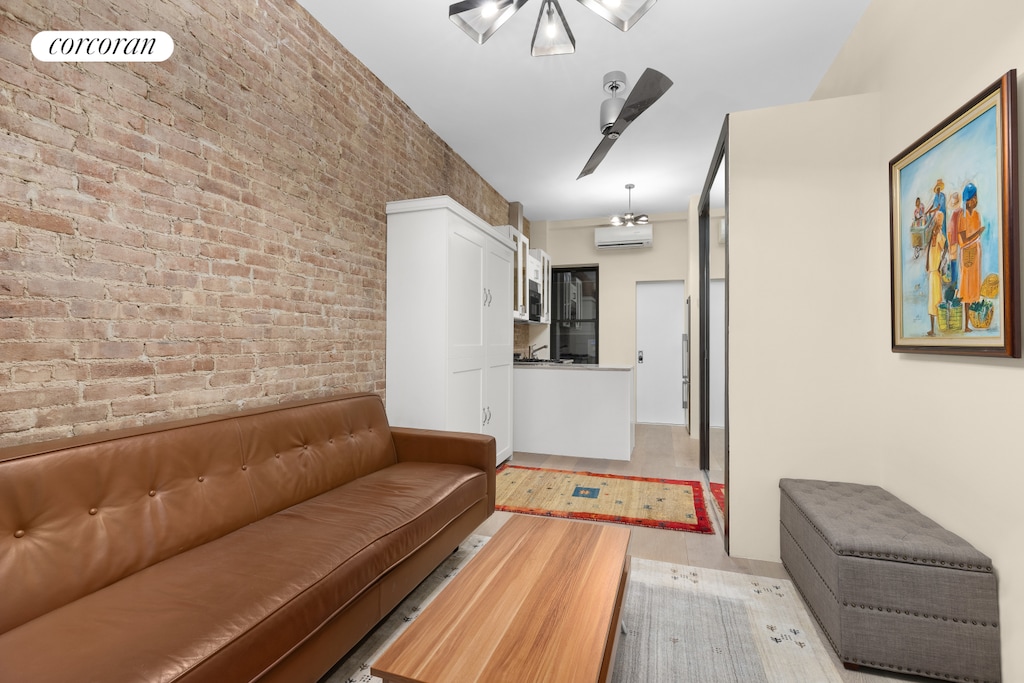 living room featuring a ceiling fan, brick wall, a wall unit AC, and light wood-style floors
