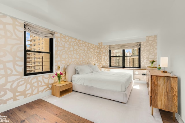 bedroom featuring wallpapered walls, wood finished floors, and baseboards