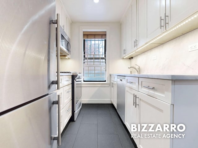 kitchen with white cabinets, dark tile patterned floors, appliances with stainless steel finishes, and baseboards