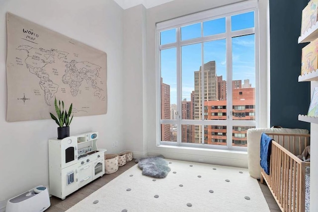 bedroom with a view of city, a nursery area, and wood finished floors