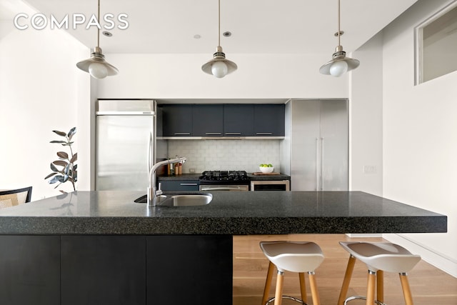 kitchen featuring a sink, tasteful backsplash, a breakfast bar area, stainless steel built in fridge, and gas range oven