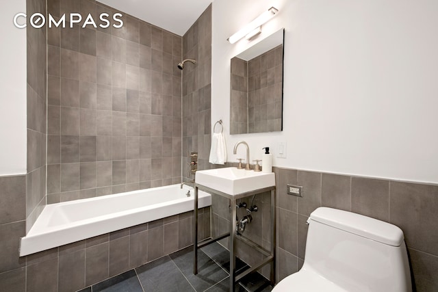 full bathroom featuring tile patterned floors, toilet, a sink, tile walls, and tiled shower / bath combo