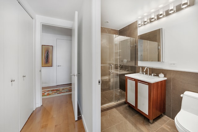 full bathroom featuring a shower stall, vanity, toilet, wood finished floors, and tile walls