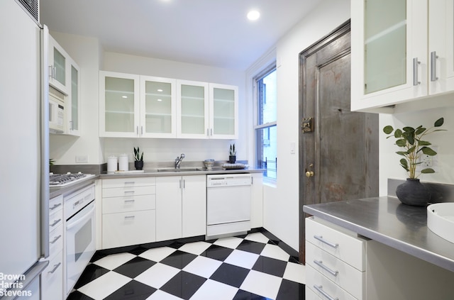 kitchen featuring white appliances, dark floors, stainless steel counters, white cabinetry, and a sink