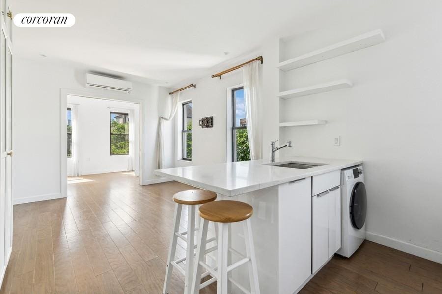 kitchen featuring washer / dryer, an AC wall unit, a sink, hardwood / wood-style flooring, and light countertops