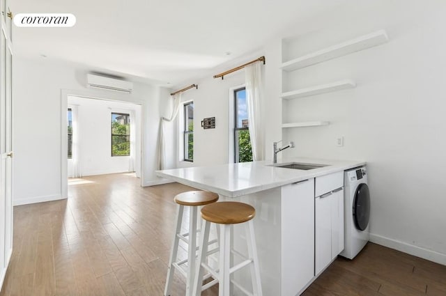 kitchen featuring washer / dryer, an AC wall unit, a sink, hardwood / wood-style flooring, and light countertops