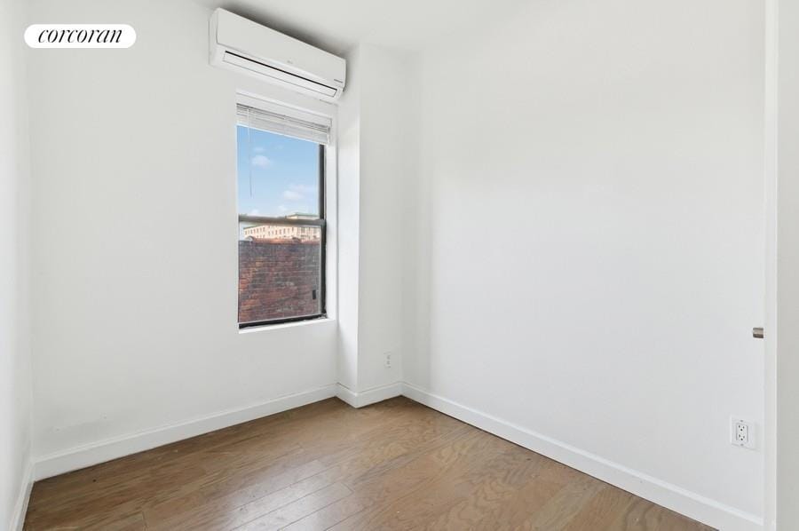 unfurnished room with a wall mounted AC, wood finished floors, and baseboards