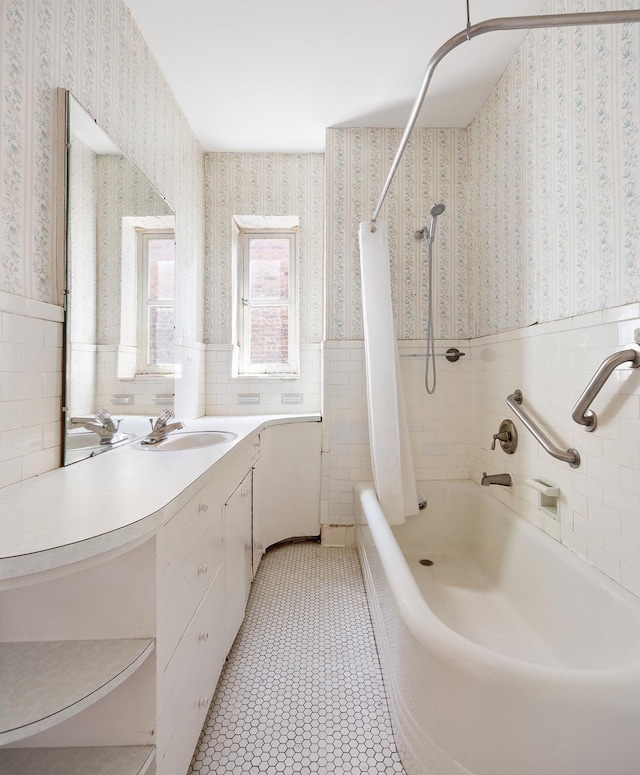 bathroom featuring wallpapered walls, tile walls, shower / bath combo with shower curtain, and wainscoting