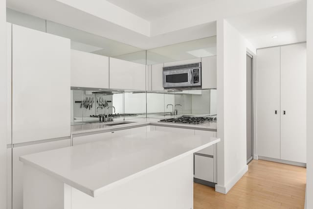 kitchen with appliances with stainless steel finishes, a sink, light wood-type flooring, and light countertops