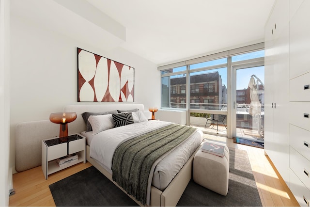 bedroom with light wood-type flooring, access to outside, and a city view