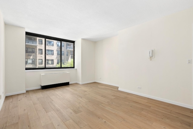 spare room featuring radiator, baseboards, and light wood-style flooring