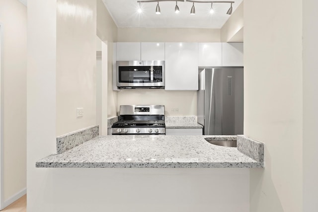 kitchen featuring modern cabinets, track lighting, light stone counters, stainless steel appliances, and white cabinetry