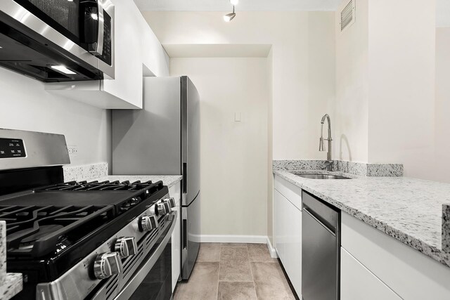 kitchen featuring visible vents, light stone countertops, white cabinetry, a sink, and appliances with stainless steel finishes